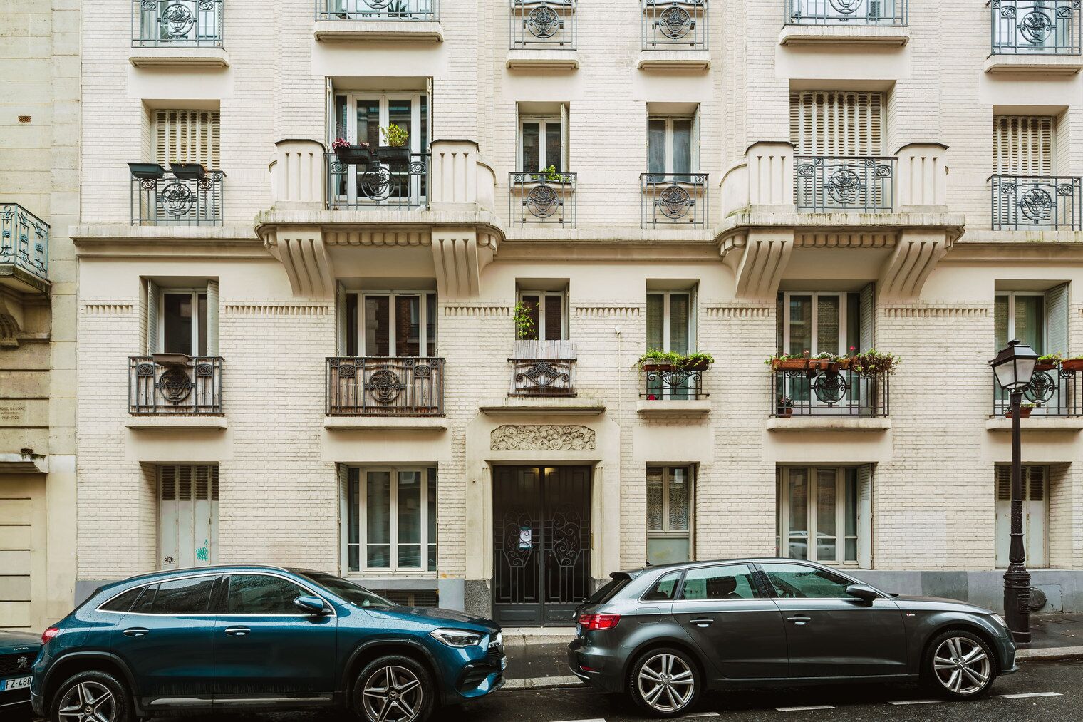 Un edificio de varios pisos con balcones, una entrada central y coches estacionados.