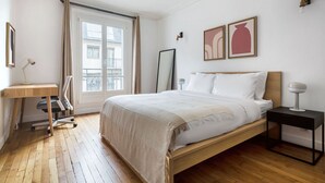 A bedroom with a wooden bed, a desk, a chair, a bedside table, and a window with curtains. - Blueground | Lamarck - Caulaincourt, nr dining (Paris)