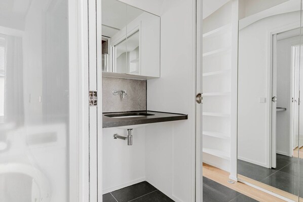 A modern bathroom with a black countertop sink, a mirror above it, and a door leading to another room.
