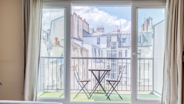 Ein Zimmer mit großem Fenster und Blick auf einen Innenhof, der zwei Holzstühle und einen kleinen Tisch zeigt.
