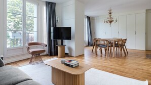 Una sala moderna con un sofá, una mesa de centro, un televisor, una mesa de comedor con sillas y una araña.