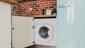 Kompakti pyykinhuoltotila, jossa on etukuormitettava pesukone, tiiliseinä ja pieni hylly, jossa on pyykinhoitotarvikkeita.