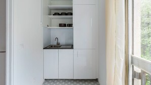 Une cuisine de taille réduite, avec des meubles blancs, un évier et une fenêtre donnant sur un espace verdoyant.