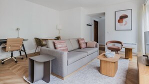 Un salon moderne avec un canapé gris, une petite table ronde, un fauteuil marron et un téléviseur.