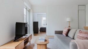 Un salon moderne avec un téléviseur à écran plat, un meuble TV en bois, un canapé gris agrémenté de coussins à motifs, une petite table basse en bois et une lampe.