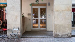 Une entrée d’immeuble avec une porte en verre, un petit seuil et une chaise à l’extérieur.