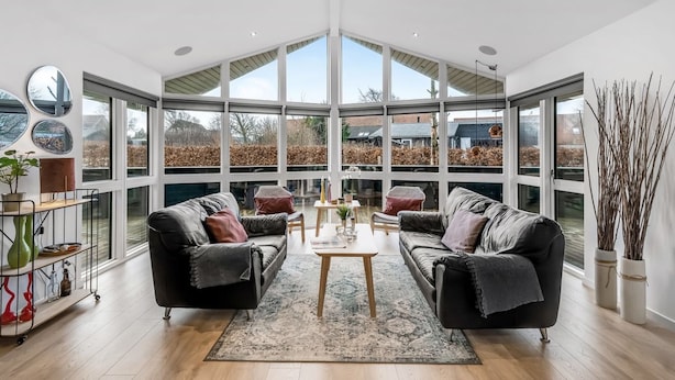 A spacious living room with two black leather sofas, a wooden coffee table, and a large window providing a view of the outdoors.