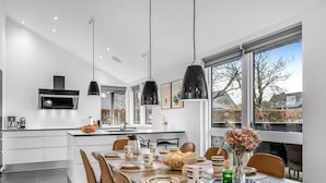 A modern kitchen with a central island, pendant lighting, and large windows offering a view of the outdoors.