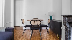 A modern living room with a wooden herringbone floor, a round table with two chairs, a sofa, a fireplace, and a door leading to another room.