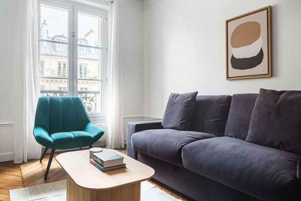 A living room with a teal armchair, a dark grey sofa, and a small wooden coffee table with books.