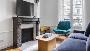 A living room with a fireplace, a television, a teal armchair, and a sofa.