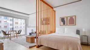 A modern hotel room with a large bed, a wooden partition, a balcony with a view, and a small seating area. - Blueground | Champ de Mars, furnished & equipped (Paris)