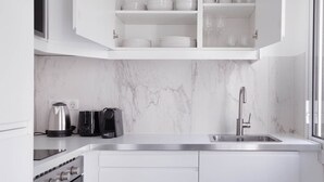 A modern kitchen with white cabinetry, a marble backsplash, a stainless steel sink, and a coffee maker. - Blueground | Champ de Mars, furnished & equipped (Paris)
