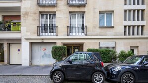 Une voiture noire est garée devant un immeuble dont le portail du garage est fermé et sur lequel est apposé un panneau indiquant qu’il est interdit de se garer.