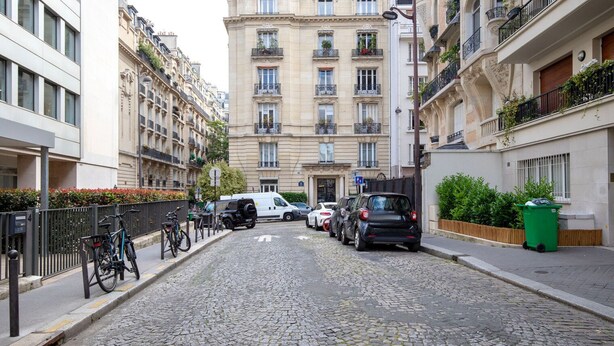 Une rue pavée bordée d’immeubles à plusieurs étages, de voitures garées et de vélos.