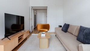 Un salon moderne avec un téléviseur à écran plat, des meubles en bois, un canapé beige et une petite table basse.