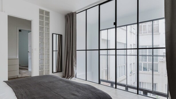A bedroom with a large window, a bed, a wardrobe, and a mirror. - Blueground | Passy, move-in-ready + furniture (Paris)