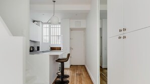 A modern kitchen with a bar stool, wooden flooring, and white cabinetry. - Blueground | Passy, move-in-ready + furniture (Paris)