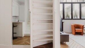 A modern interior with a wooden floor, white walls, and a staircase leading to a loft area. - Blueground | Passy, move-in-ready + furniture (Paris)