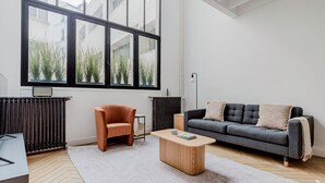 A modern living room with a large window, a grey sofa, an orange armchair, and a wooden coffee table. - Blueground | Passy, move-in-ready + furniture (Paris)