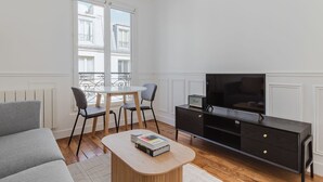 A modern living room with a sofa, a round coffee table, a TV, and a dining area with chairs and a table. - Blueground | Pasteur - Montparnasse, furnished (Paris)