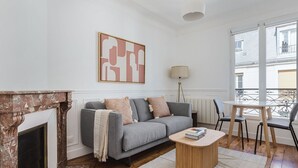 A living room with a fireplace, grey sofa, coffee table, and a view of the outside. - Blueground | Pasteur - Montparnasse, furnished (Paris)