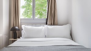 Un dormitorio con cama, lámpara de noche y ventana con cortinas.