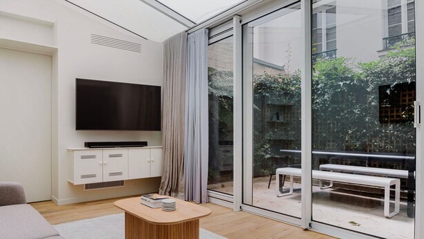 Een moderne woonkamer met een flatscreen-televisie, een houten salontafel en een schuifdeur naar een buiten zitgedeelte.