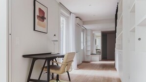 Een hal met een bureau en stoel, witte wanden en houten vloer.