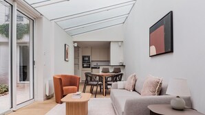 Een moderne woonkamer met een bank, fauteuil, salontafel en een eethoek met stoelen en een tafel.