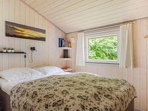 Een slaapkamer met een bed, een raam met gordijnen, een boekenkast en een schilderij aan de muur.