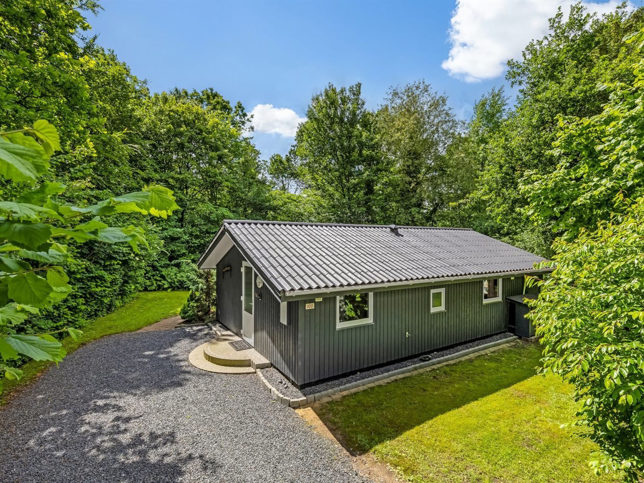 A small, single-story building with a metal roof, surrounded by lush greenery.
