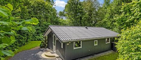 A small, single-story building with a metal roof, surrounded by lush greenery.