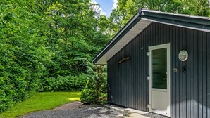 A small, dark-colored building with a white door, surrounded by a gravel driveway and lush greenery. - "Gorica" - 30km from the sea by Interhome (Toftlund)