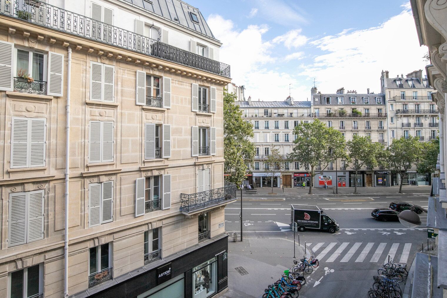 A multi-story building with balconies, a street with cars and bicycles, and storefronts.