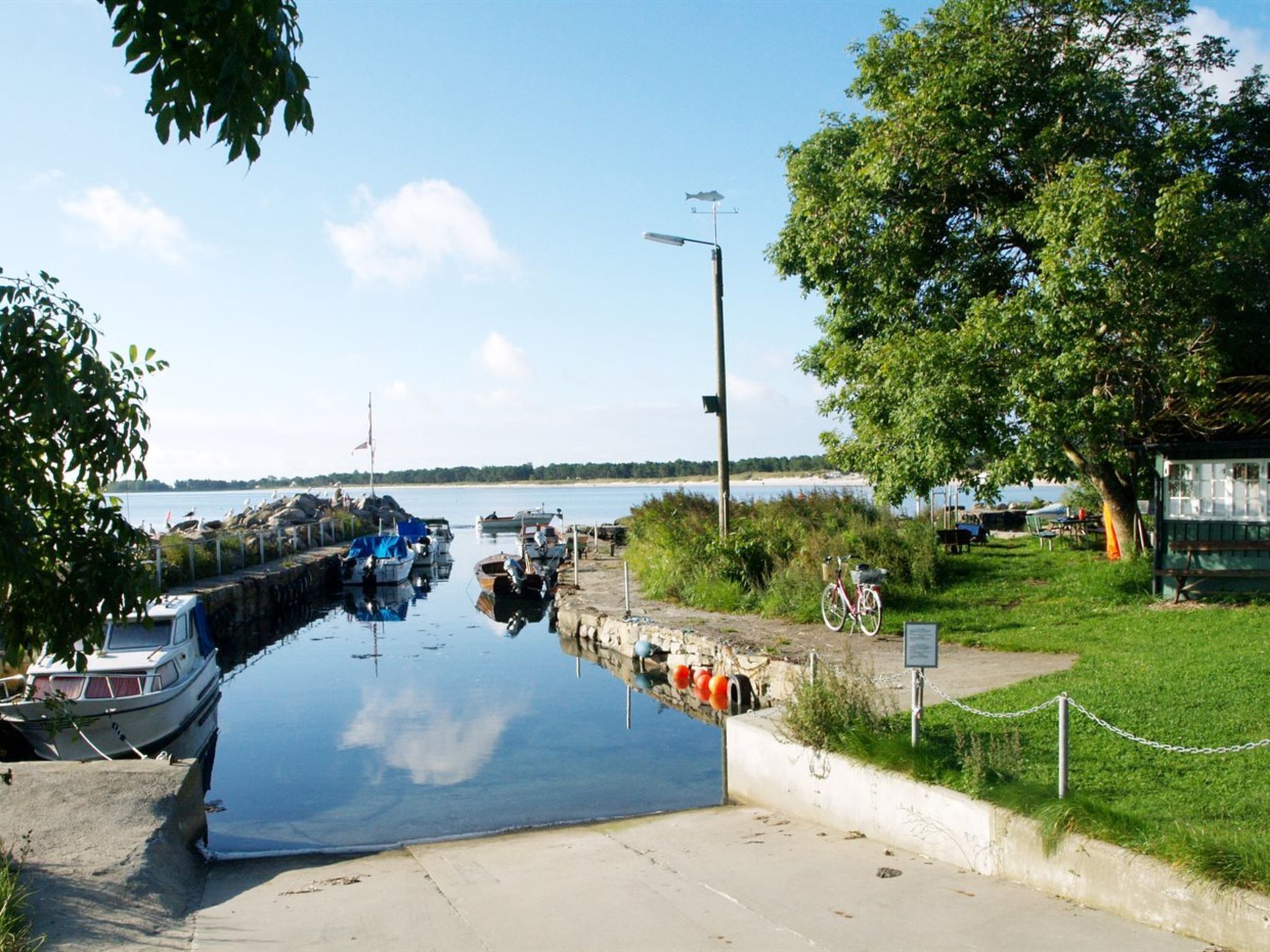 Un rivage paisible où sont amarrés des bateaux, un ciel dégagé et une zone herbeuse avec un banc.