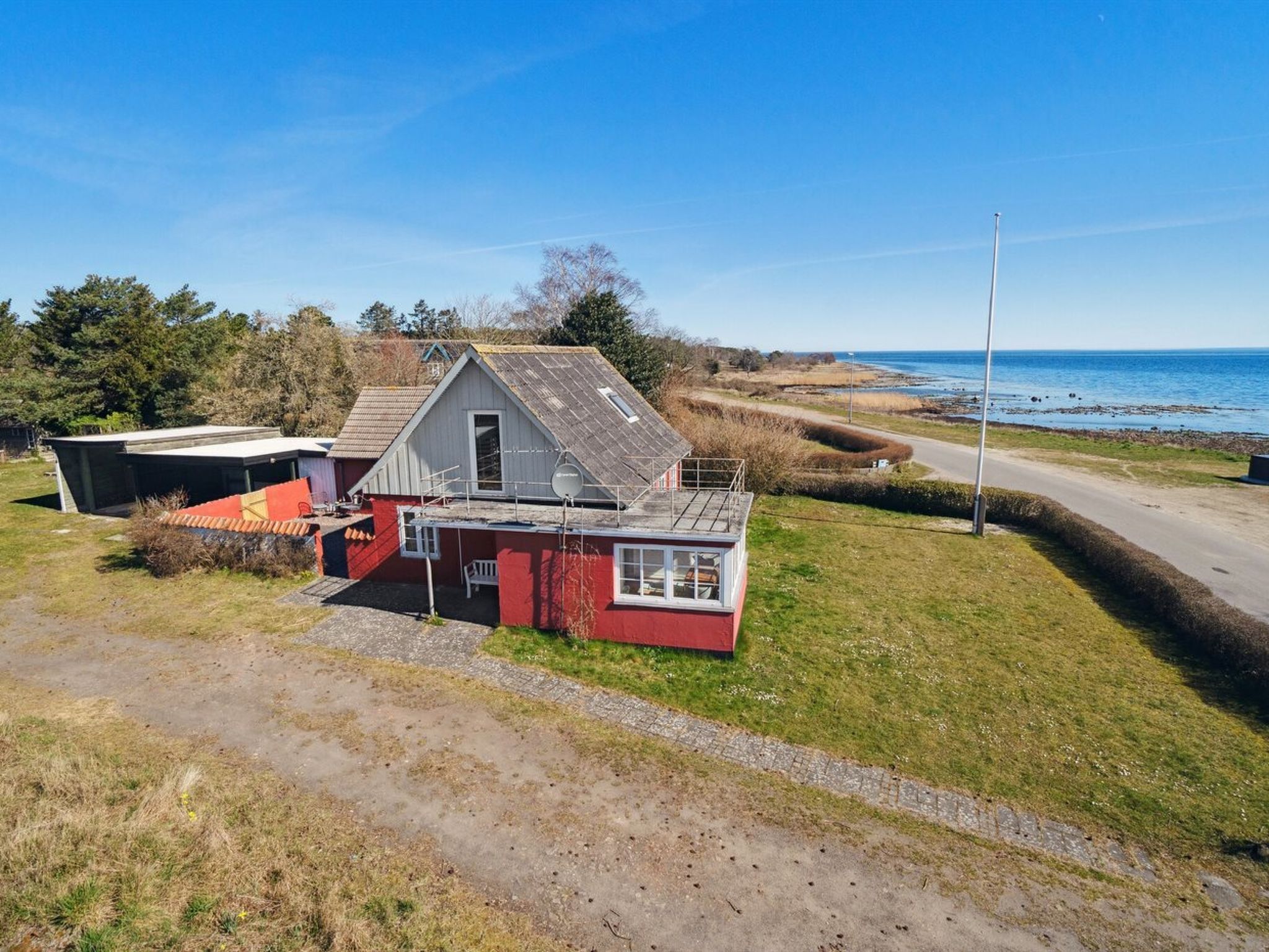 Une maison rouge et blanche avec un toit en pente, un petit porche et une vue sur la mer.