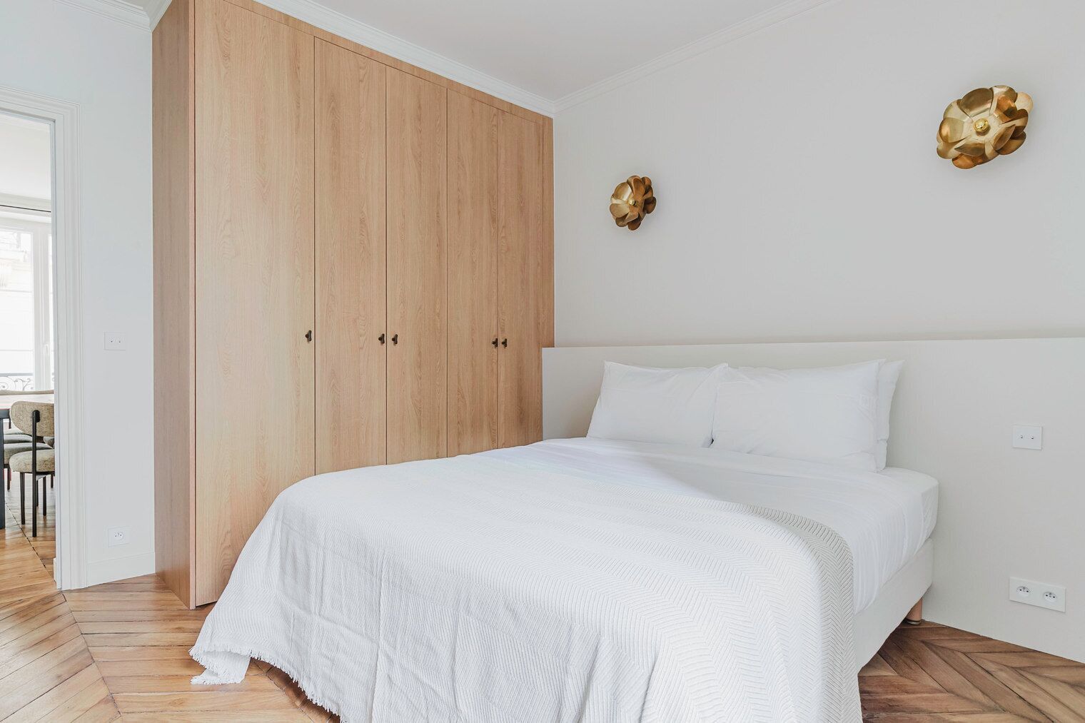 Un dormitorio con un armario grande de madera, una cama con ropa de cama blanca y dos adornos colgantes en la pared.
