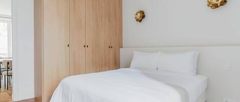 Un dormitorio con un armario grande de madera, una cama con ropa de cama blanca y dos adornos colgantes en la pared.