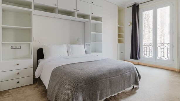 Un dormitorio con cama, armario blanco y ventana con cortinas.
