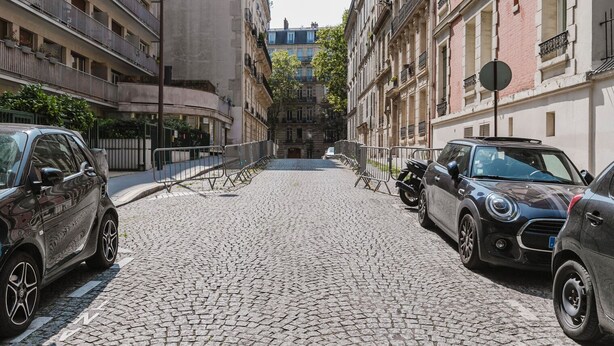 A cobblestone street lined with multi-story buildings, featuring parked cars and a visible motorcycle. - Blueground | Pereire, elevator, near Porte Mailot (Paris)
