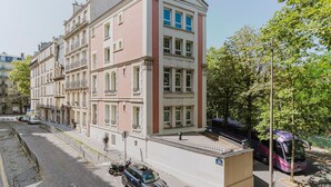 A multi-story building with a pink facade, a covered outdoor area, and a parked bus. - Blueground | Pereire, elevator, near Porte Mailot (Paris)