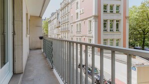 A balcony with a metal railing overlooking a street with parked cars and buildings. - Blueground | Pereire, elevator, near Porte Mailot (Paris)