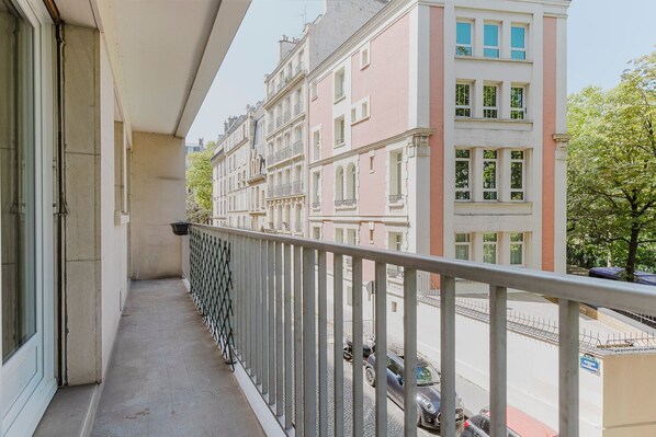 A balcony with a metal railing overlooking a street with parked cars and buildings.