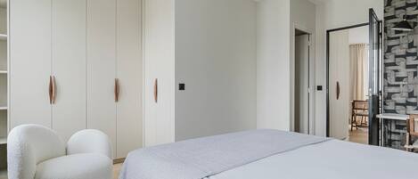 Un dormitorio con una cama, un sillón blanco, un armario y una pared decorada.