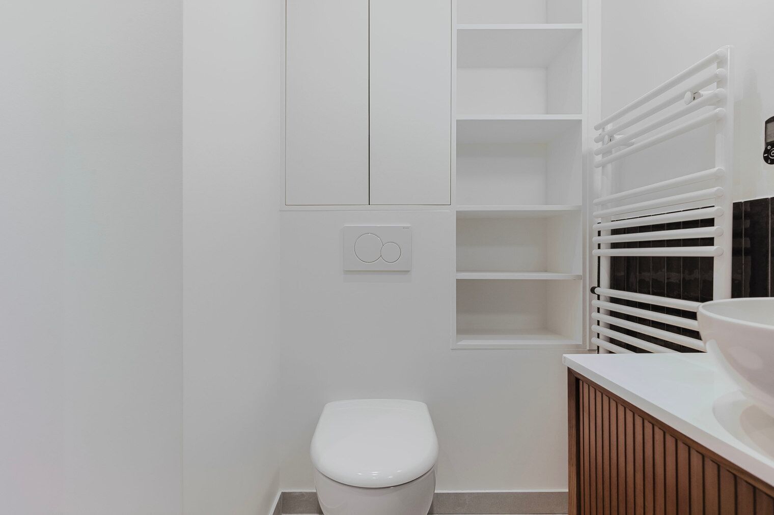 Un baño moderno con inodoro blanco, estante empotrado y perchero.