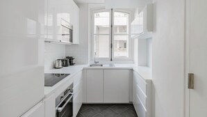 A narrow kitchen with white cabinetry, a built-in oven, and a window with a view of the outside.