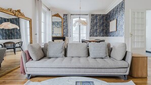 A living room with a grey sofa, patterned wallpaper, and a large mirror.