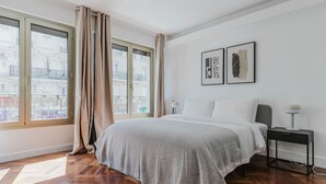 A bedroom with a large bed, a nightstand, a lamp, and two framed pictures on the wall. - Blueground | Invalides, nr embassies & museum (Paris)