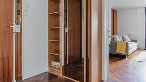 A hallway with a wooden wardrobe, a grey sofa with a yellow throw, and a radiator. - Blueground | Invalides, nr embassies & museum (Paris)